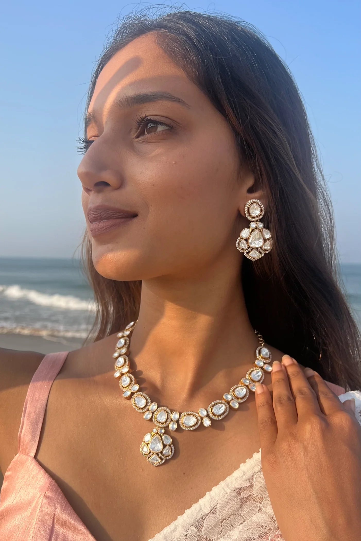 Fine jewelry close-up featuring multiple layered diamond chains paired with sparkling drop earrings against a textured gold outfit.