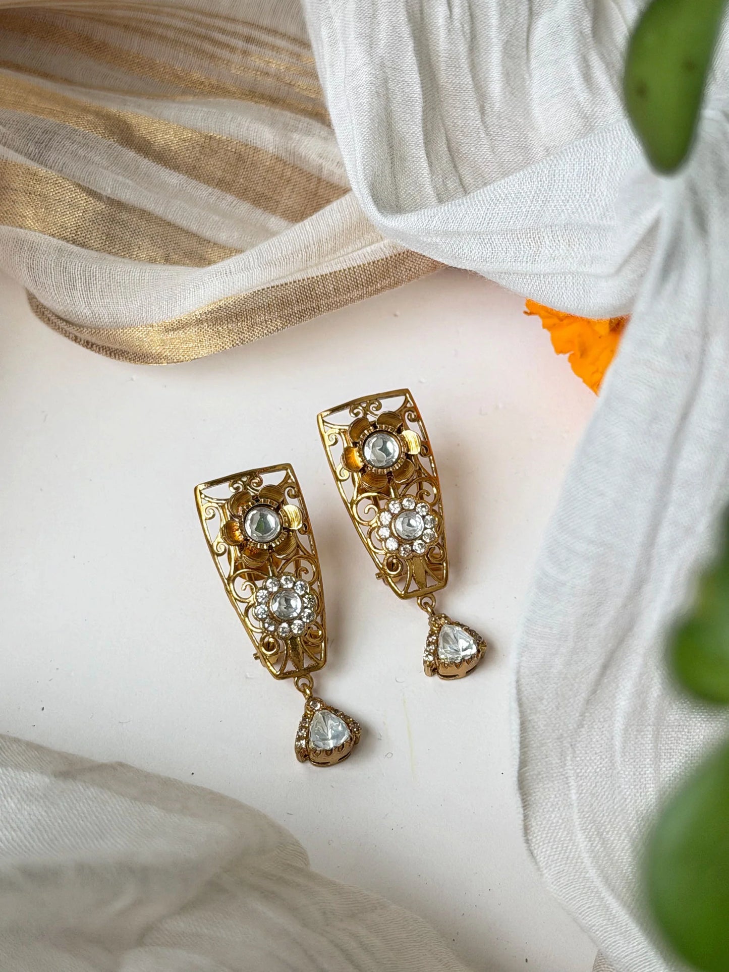Traditional gold earrings with ornate detailing and hanging crystal drops in soft lighting