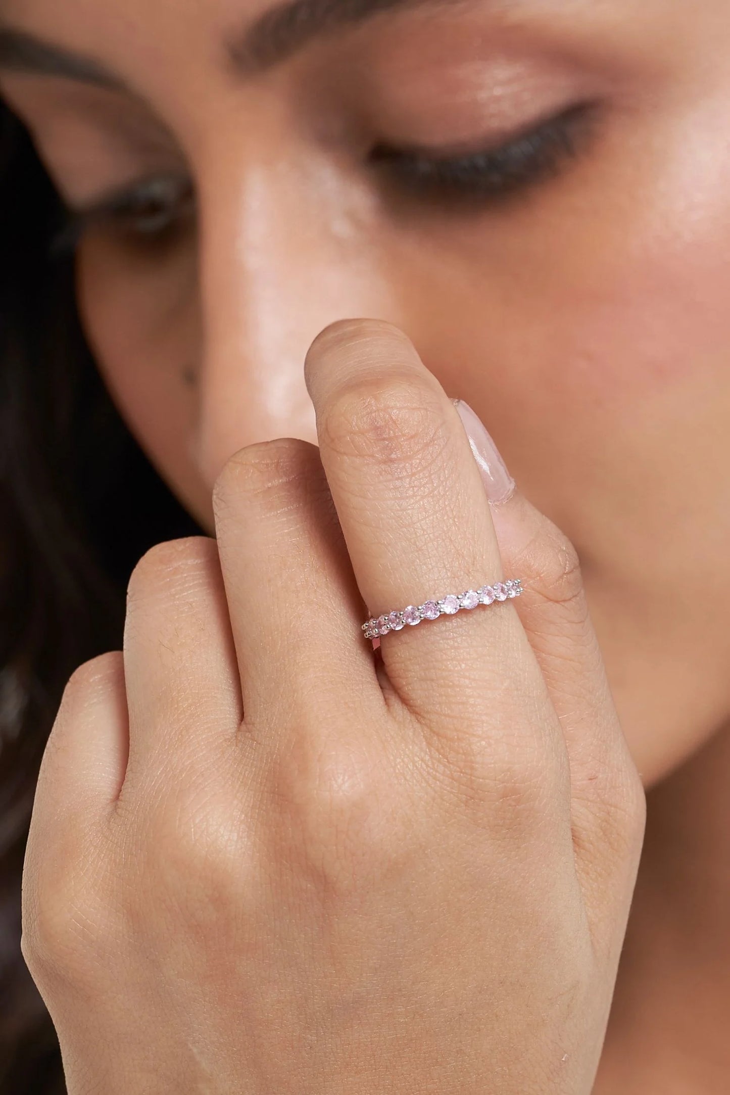 Elegant beauty shot highlighting a slim diamond ring, soft pink stud earrings, and a fine necklace on a woman in a white outfit.