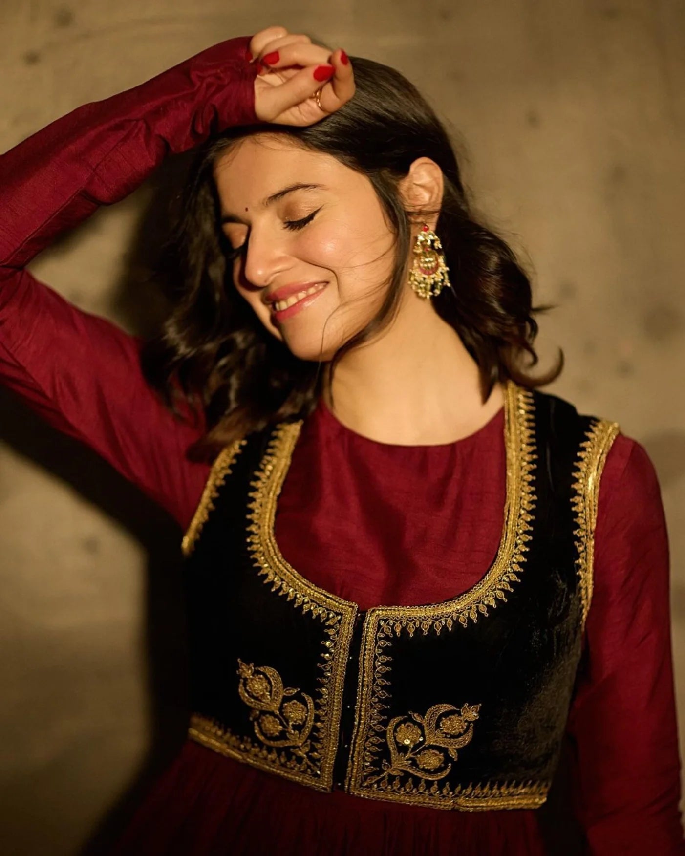 Beauty shot highlighting a woman’s joyful expression paired with detailed gold earrings and a textured red ensemble.