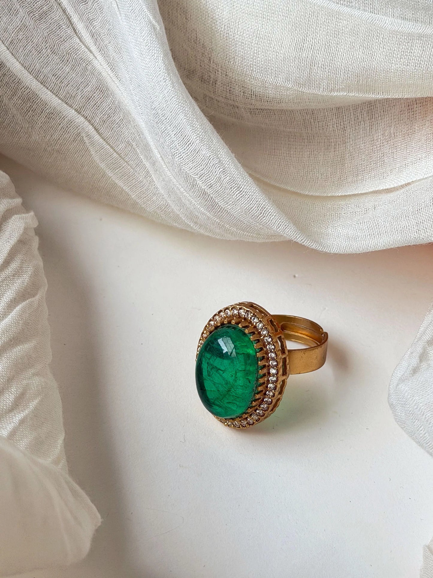 Close-up of gold ring with oval green gemstone and diamond halo on soft neutral background