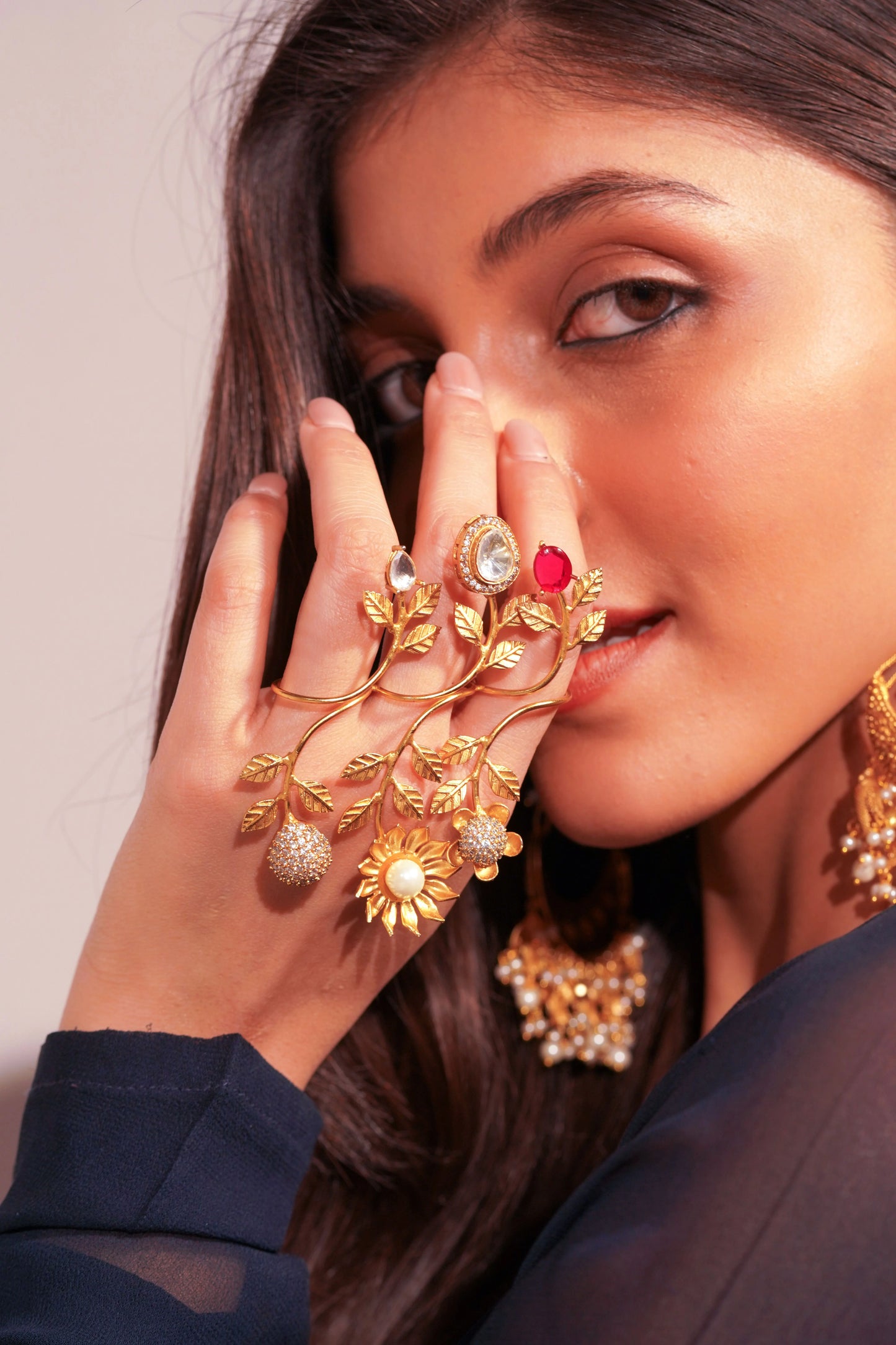 Close-up of woman wearing intricate gold hand jewelry with leaf design and gemstone rings