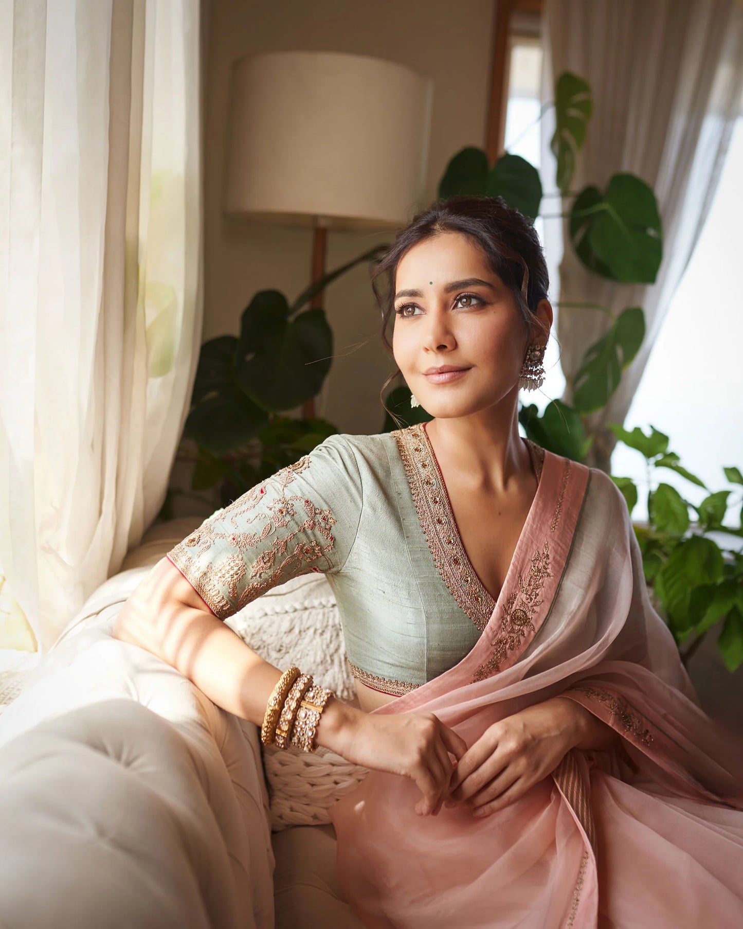 Radiant woman in pastel saree with embroidered blouse and gold jewelry captured in soft indoor lighting