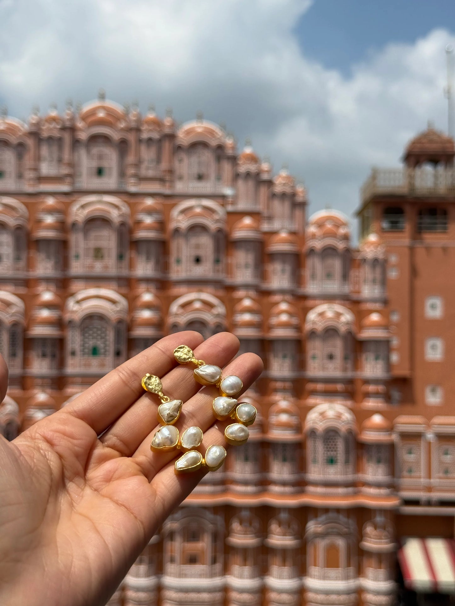 Luxury gold earrings with irregular pearl drops showcased against heritage building setting