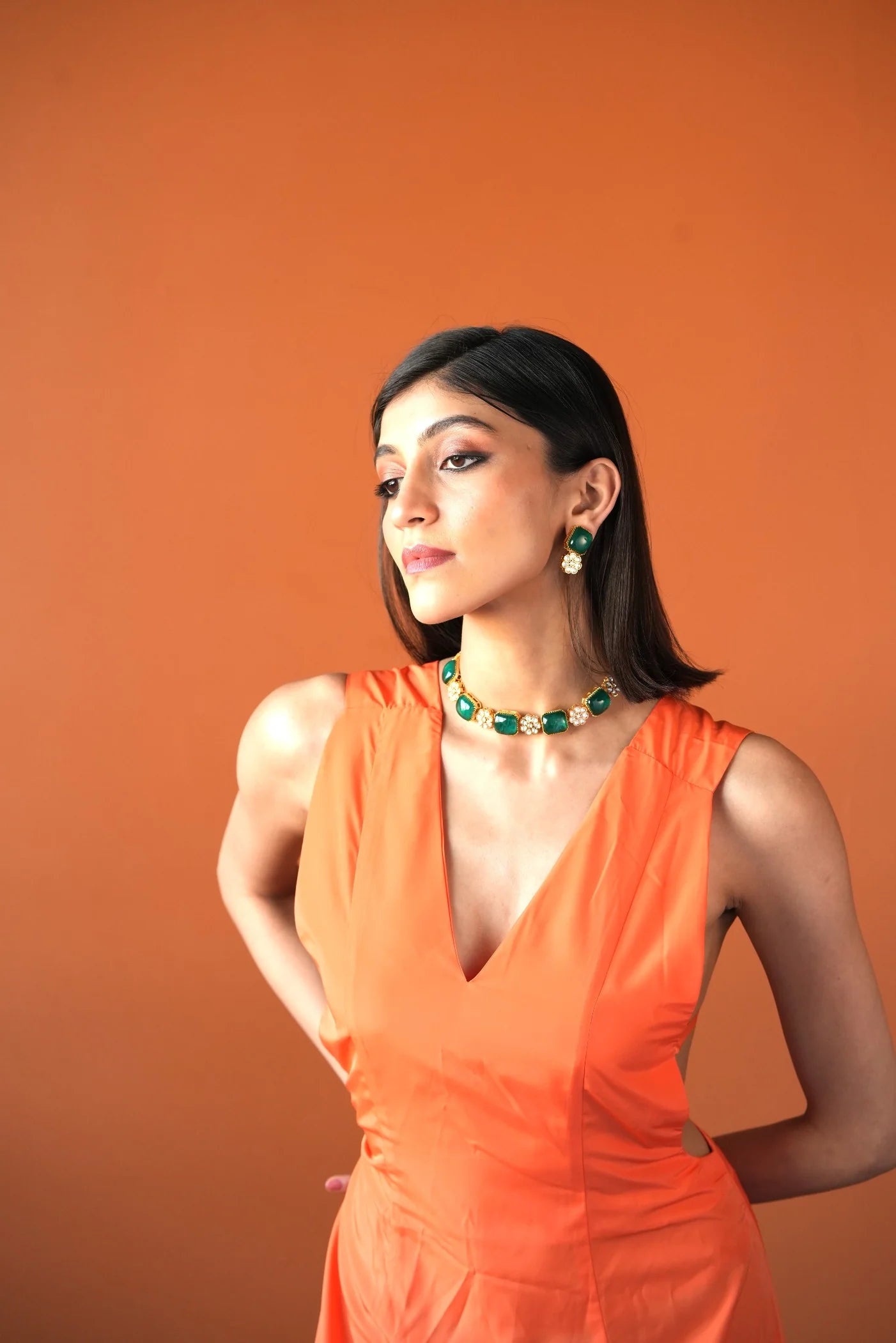 Detailed close-up of a polished green gemstone earring framed in gold with pearl embellishments, captured in soft lighting.