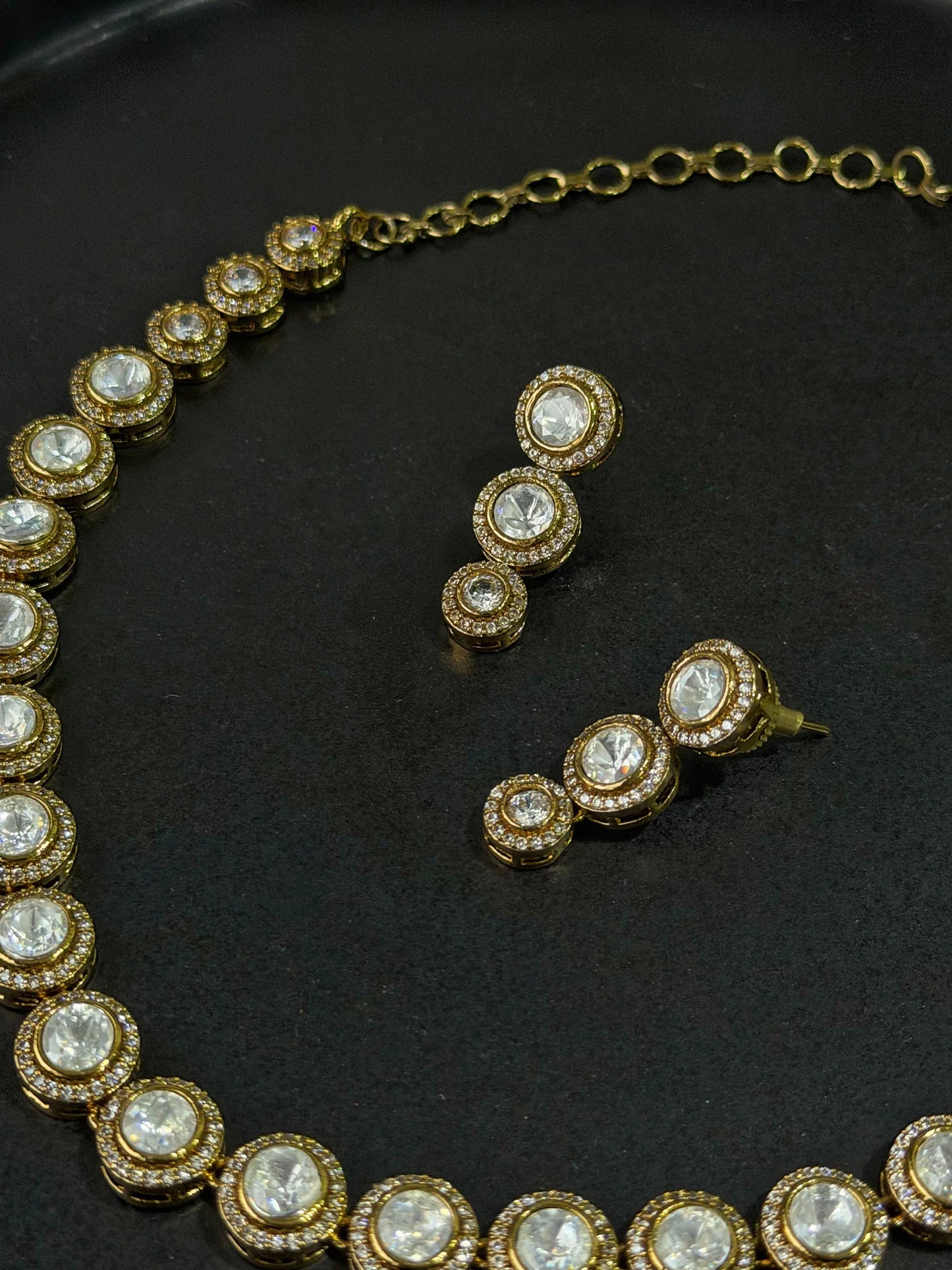 Luxury gold necklace and drop earrings set with round crystal stones on black background