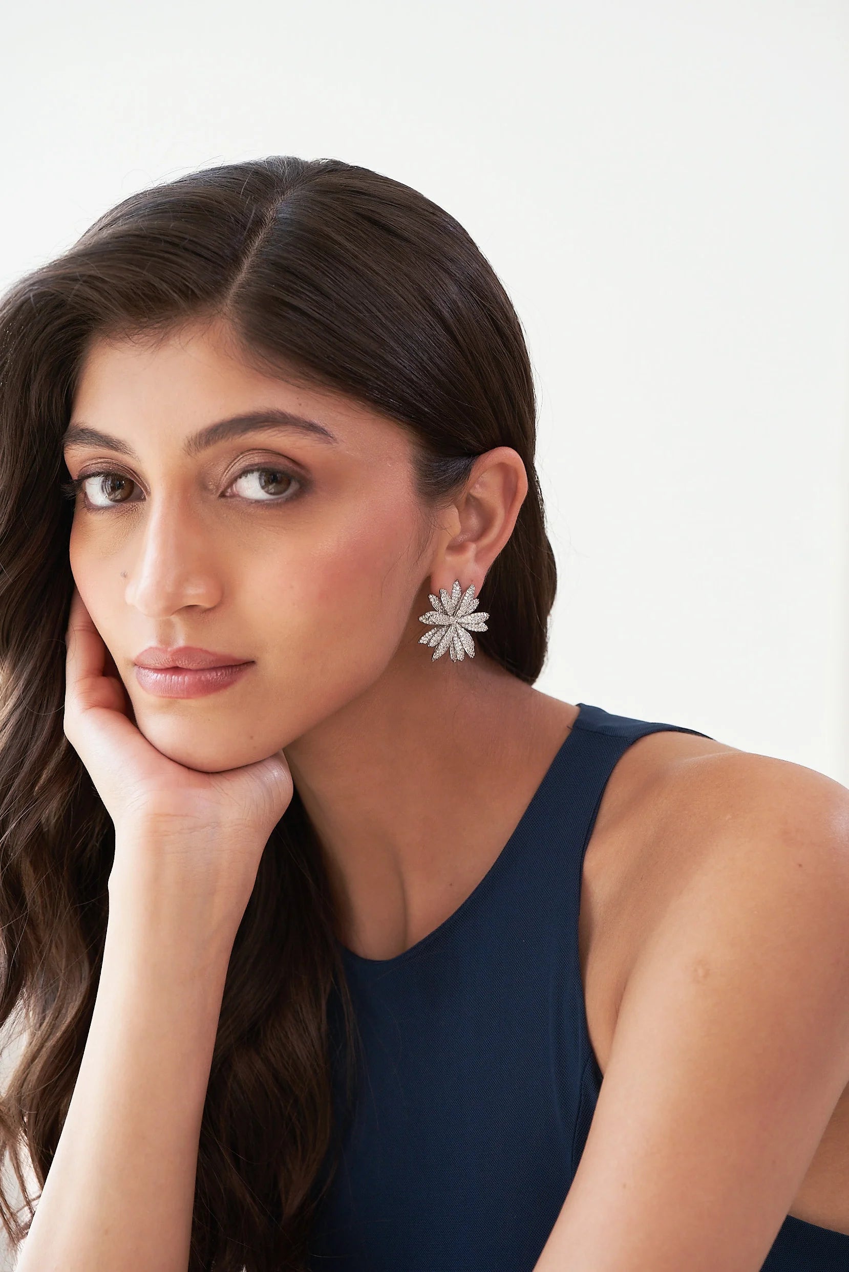 Close-up of an ear adorned with a bold, daisy-inspired silver stud earring featuring textured, crystal-covered petals.
