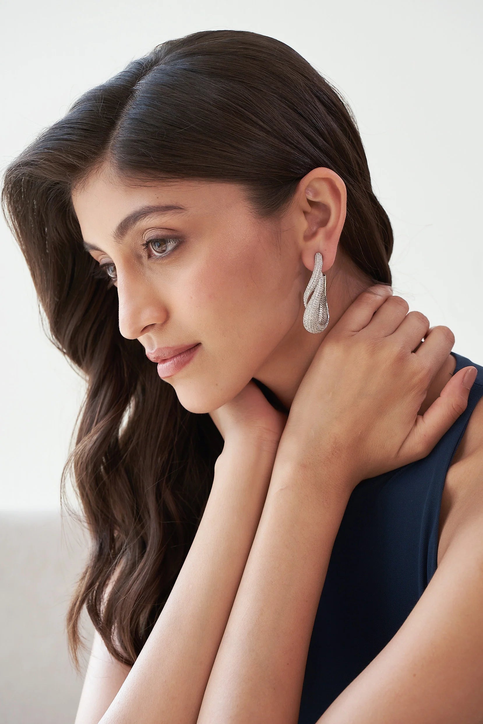Detailed view of an elegant, textured silver drop earring with intertwined curves and shimmering stones.
