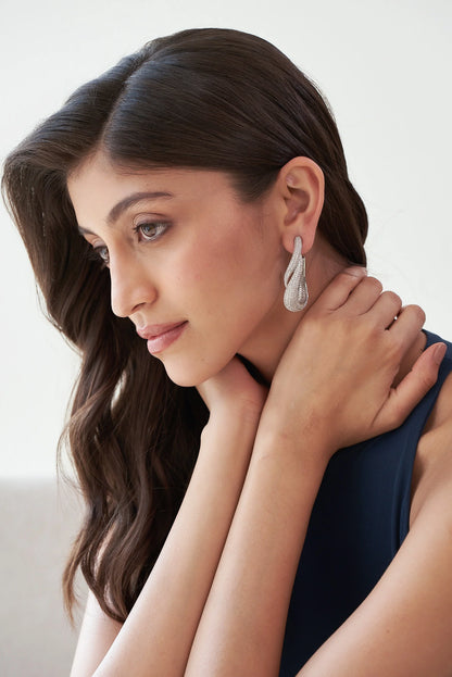 Detailed view of an elegant, textured silver drop earring with intertwined curves and shimmering stones.
