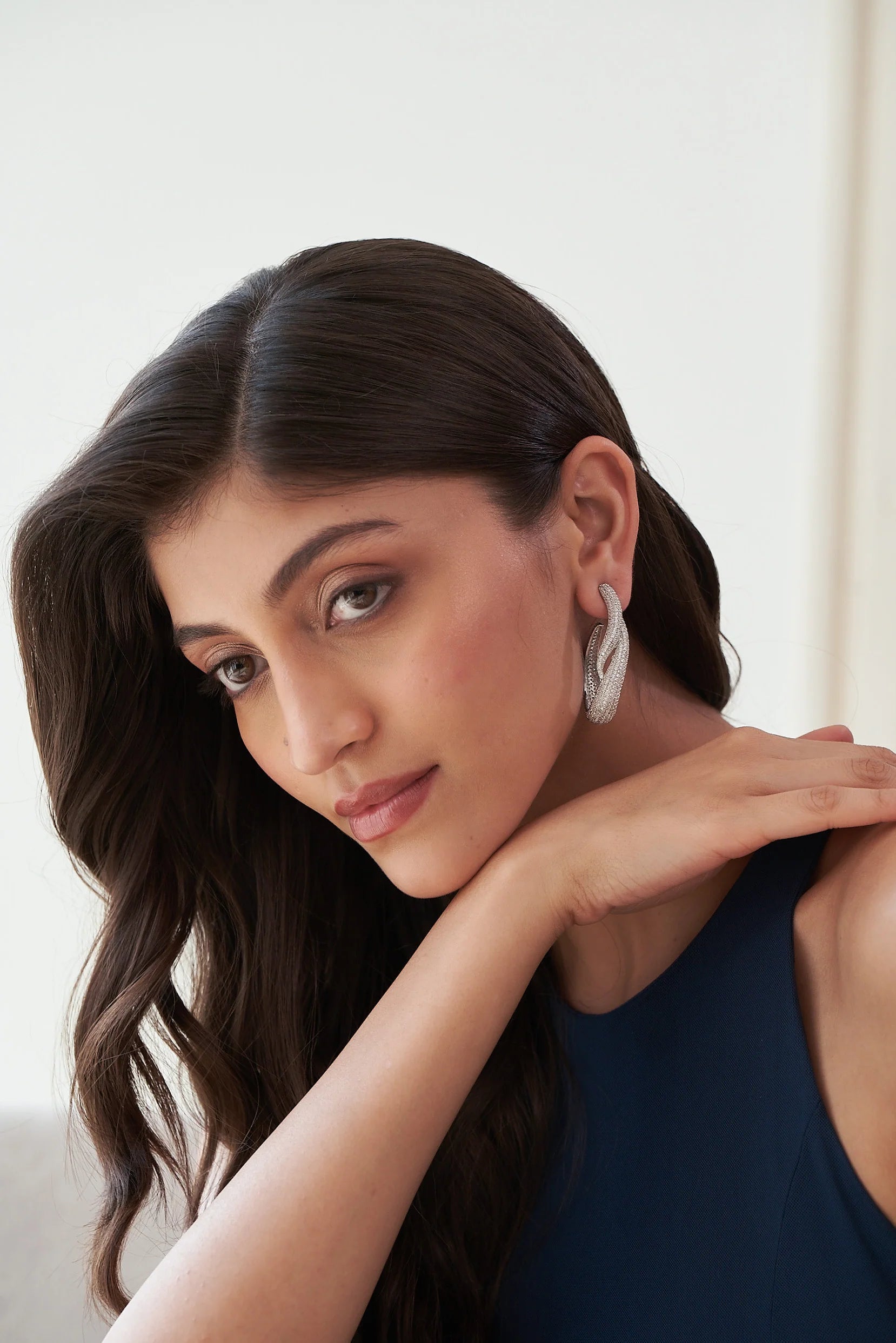 Close-up of a person’s ear wearing a modern, curved silver earring with a pavé-style surface.
