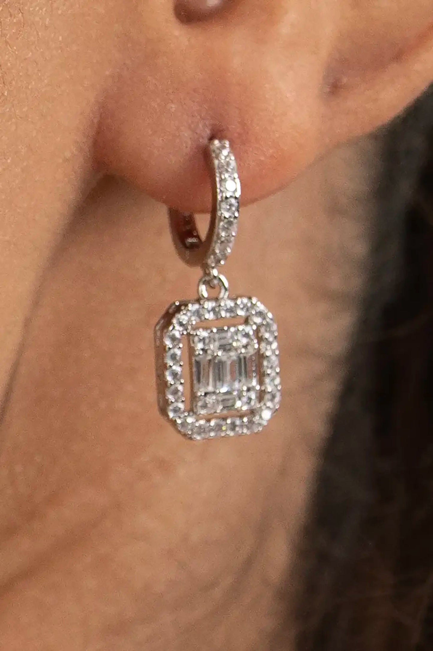 Elegant diamond drop earring with halo setting and baguette center stone, close-up jewelry detail