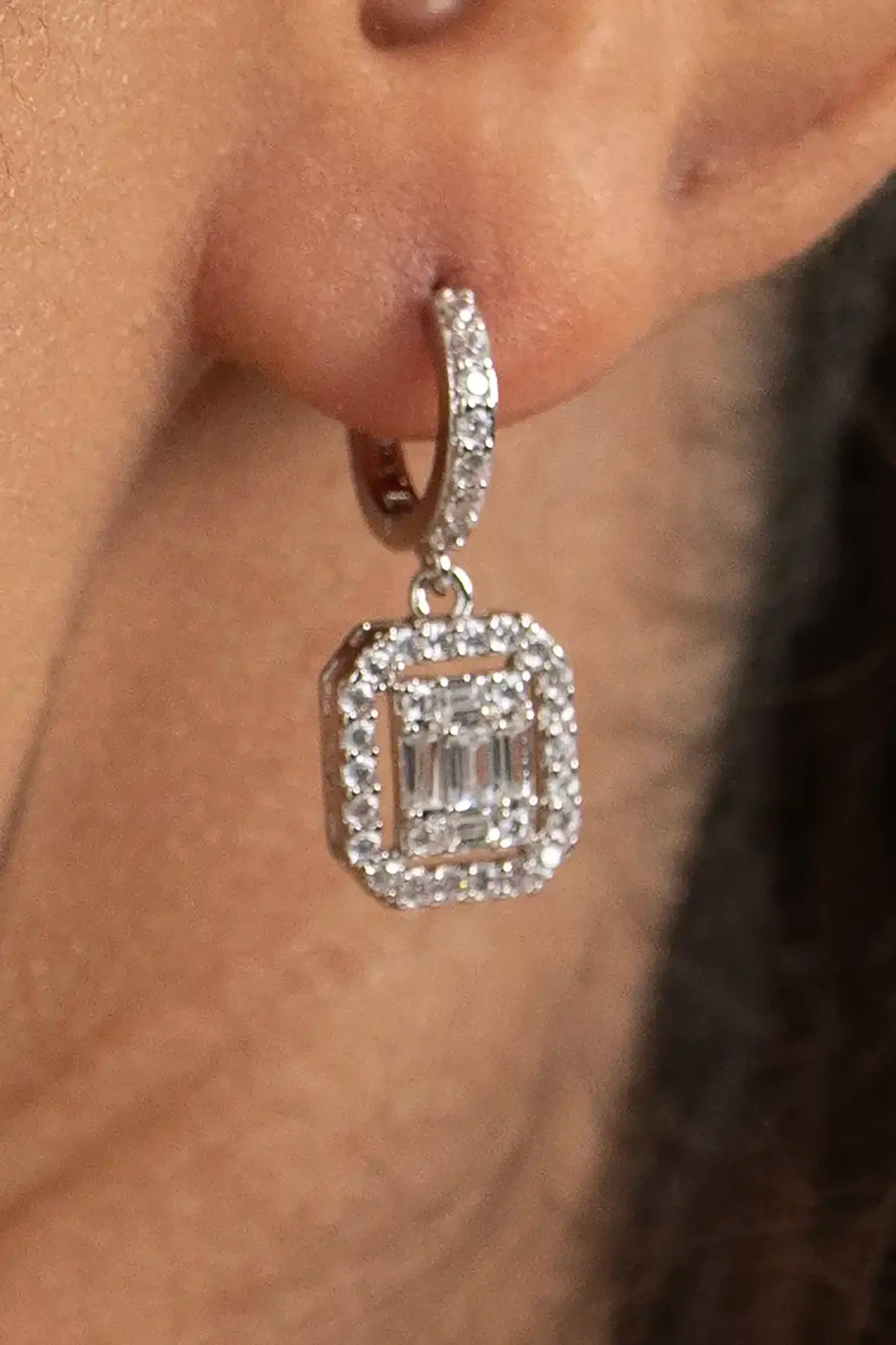 Elegant diamond drop earring with halo setting and baguette center stone, close-up jewelry detail