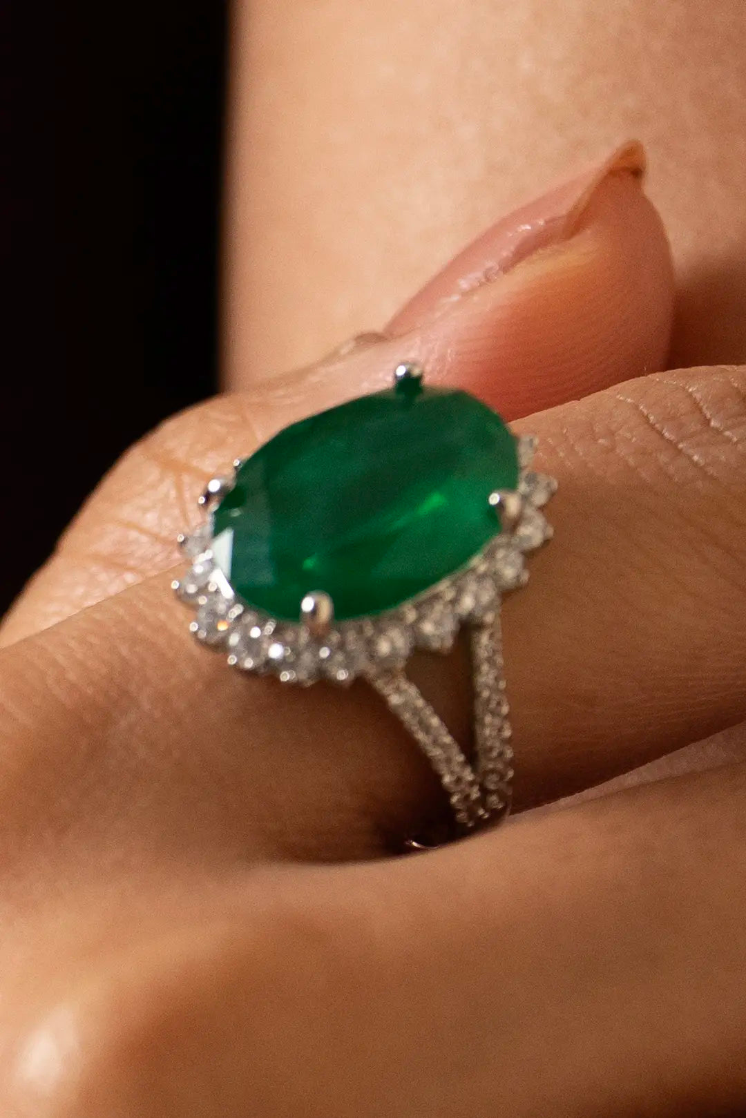 Model wearing emerald and diamond jewelry set with pendant necklace, drop earrings, bracelet and statement ring in elegant pose