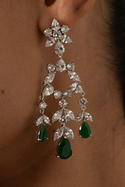 Side profile of smiling woman wearing diamond chandelier earrings with green emerald drops and matching bracelet