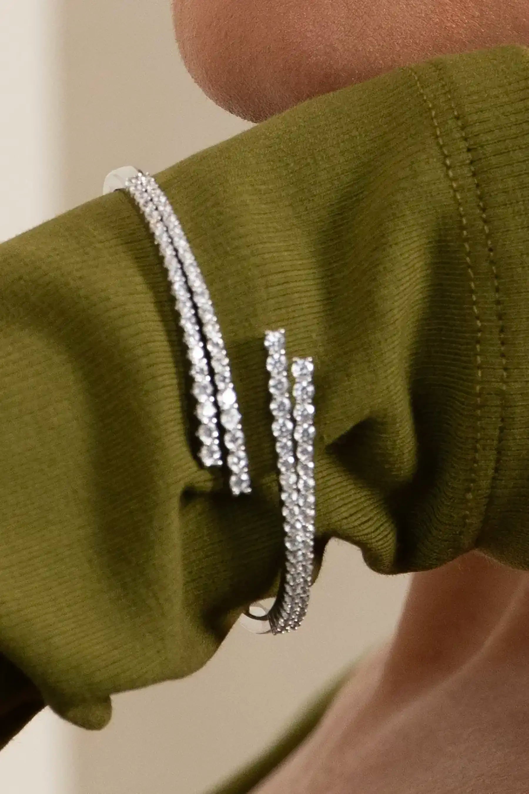 Elegant woman in green outfit wearing sparkling drop earrings and silver bracelets, showcasing modern fashion jewelry