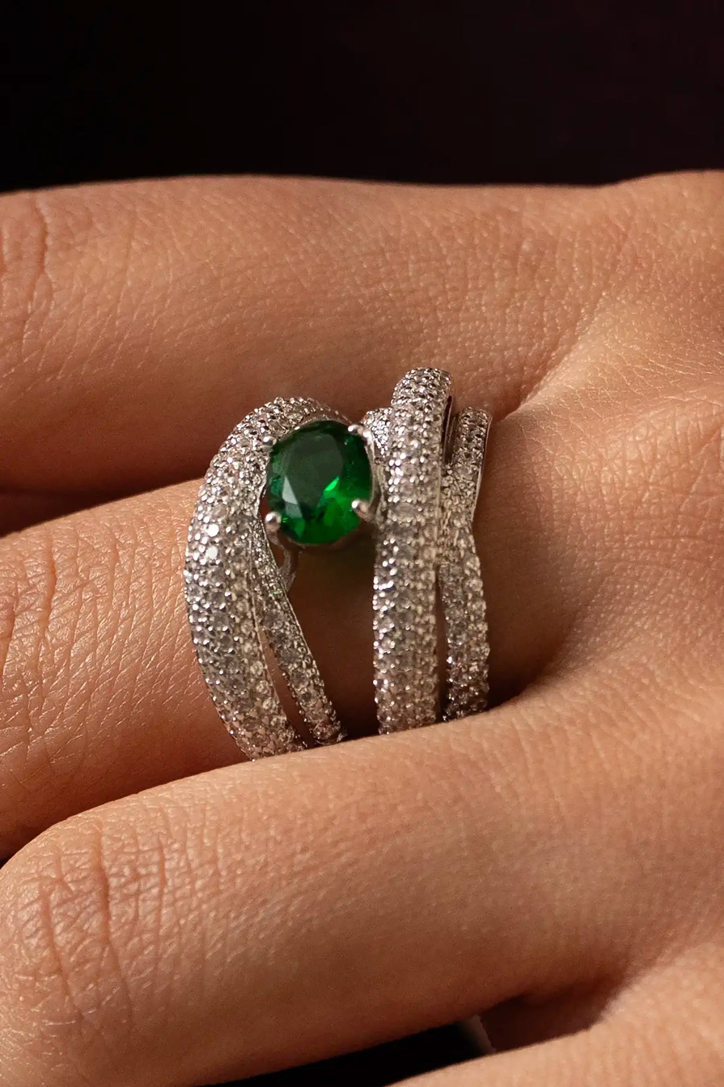 Hand wearing diamond ring with oval emerald center stone set in multi-band pavé design, elegant fine jewelry close-up