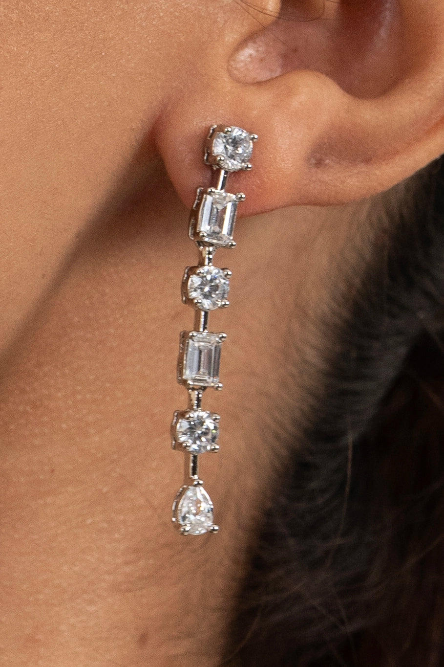 Close-up of a woman with long sleek hair wearing diamond drop earrings, highlighting luxury jewelry design