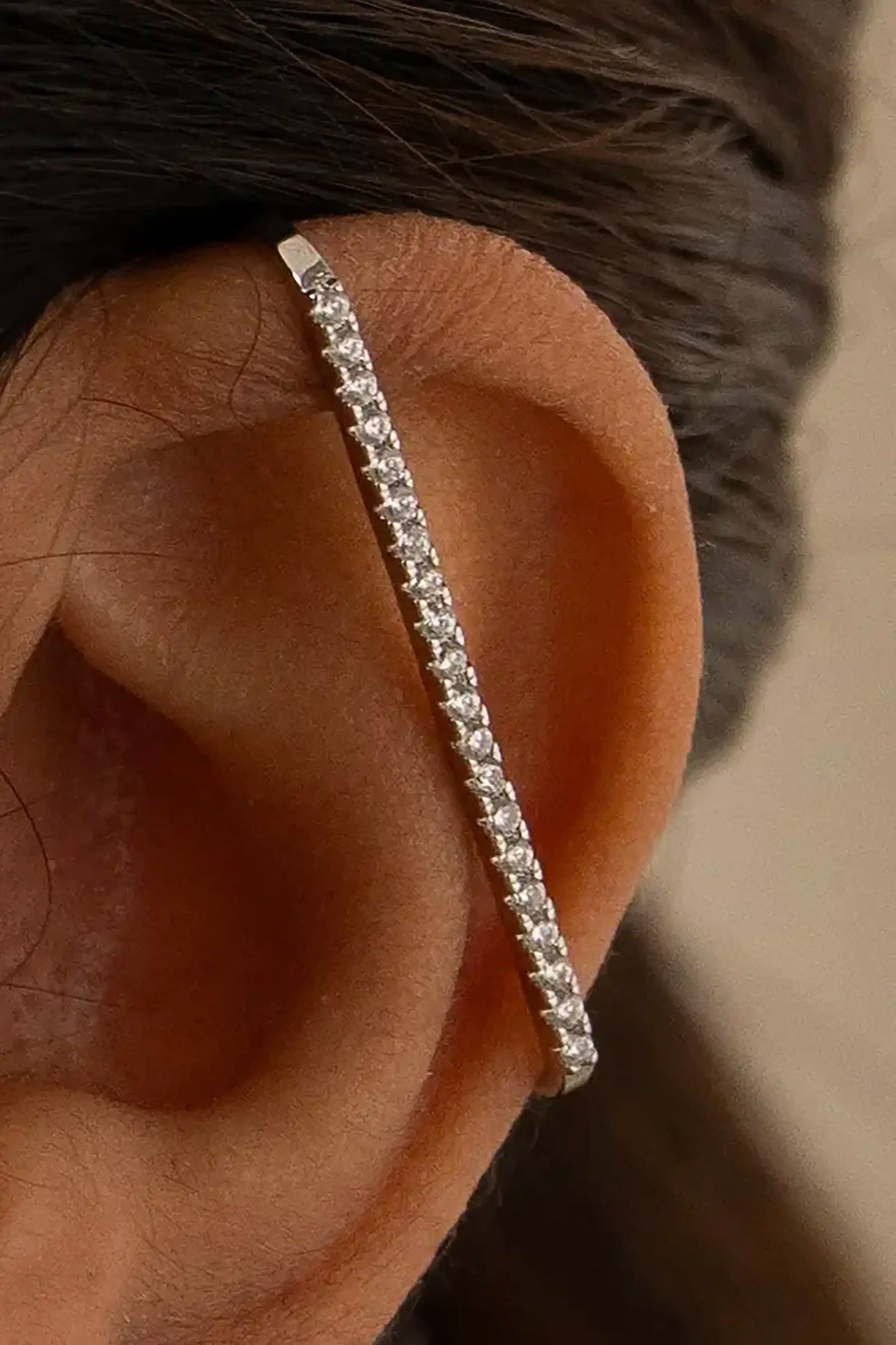 Close-up of a human ear wearing a diamond-studded silver ear cuff, showcasing modern minimalist jewelry design