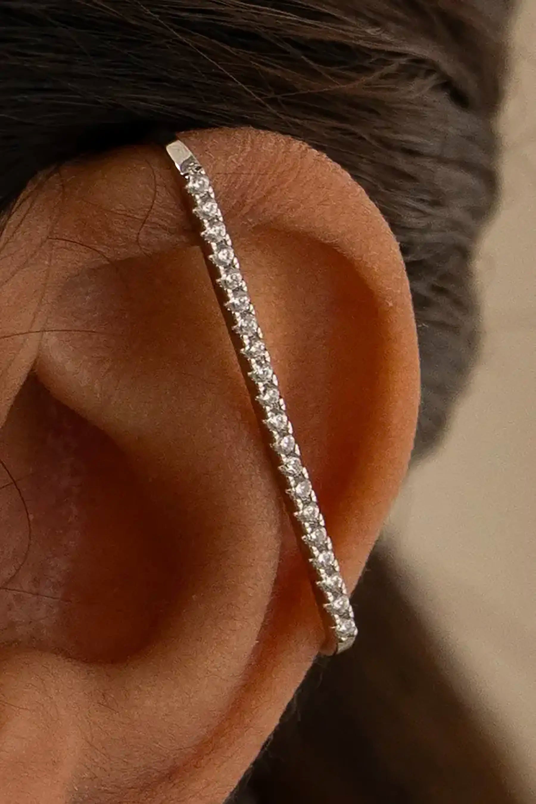 Close-up of a human ear wearing a diamond-studded silver ear cuff, showcasing modern minimalist jewelry design
