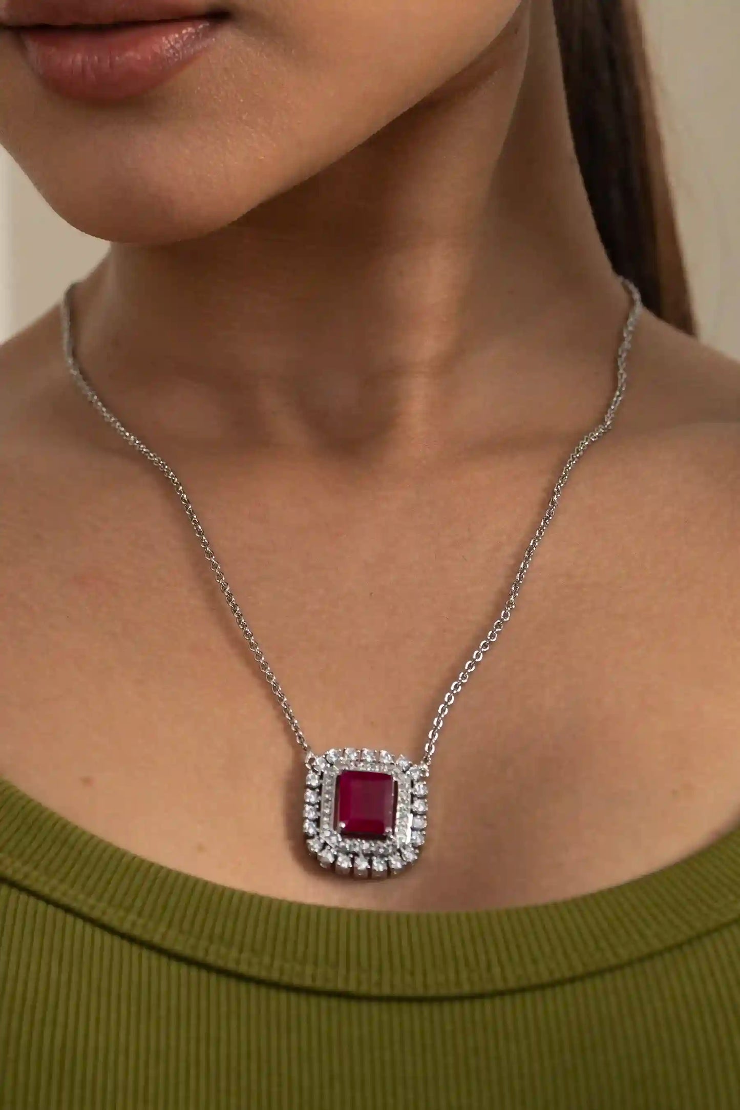 Ruby cushion halo necklace set with square-cut ruby pendant and matching diamond halo earrings on model in olive green outfit