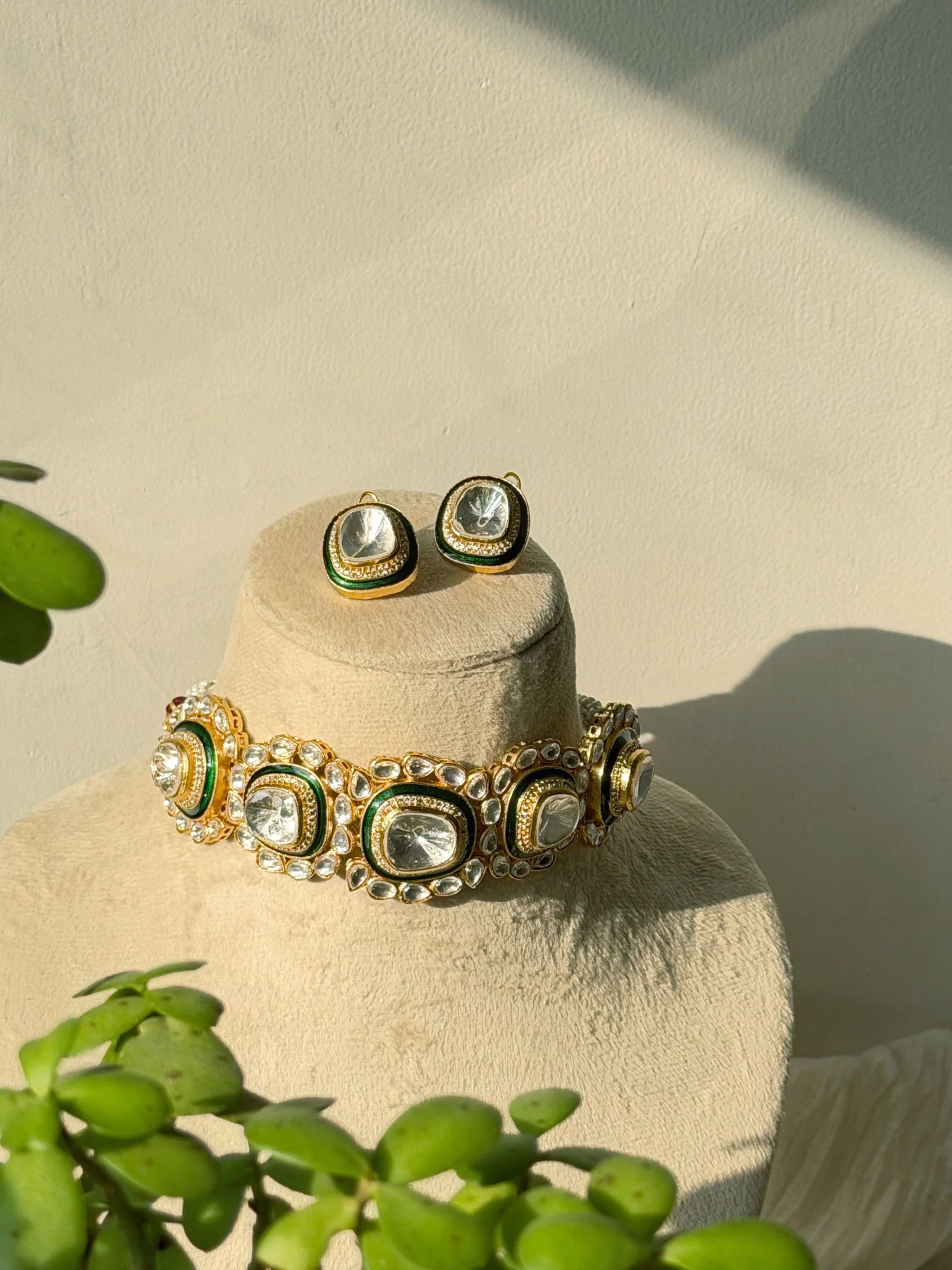 Luxury gold choker necklace with green enamel and kundan stones displayed on jewelry bust with matching earrings
