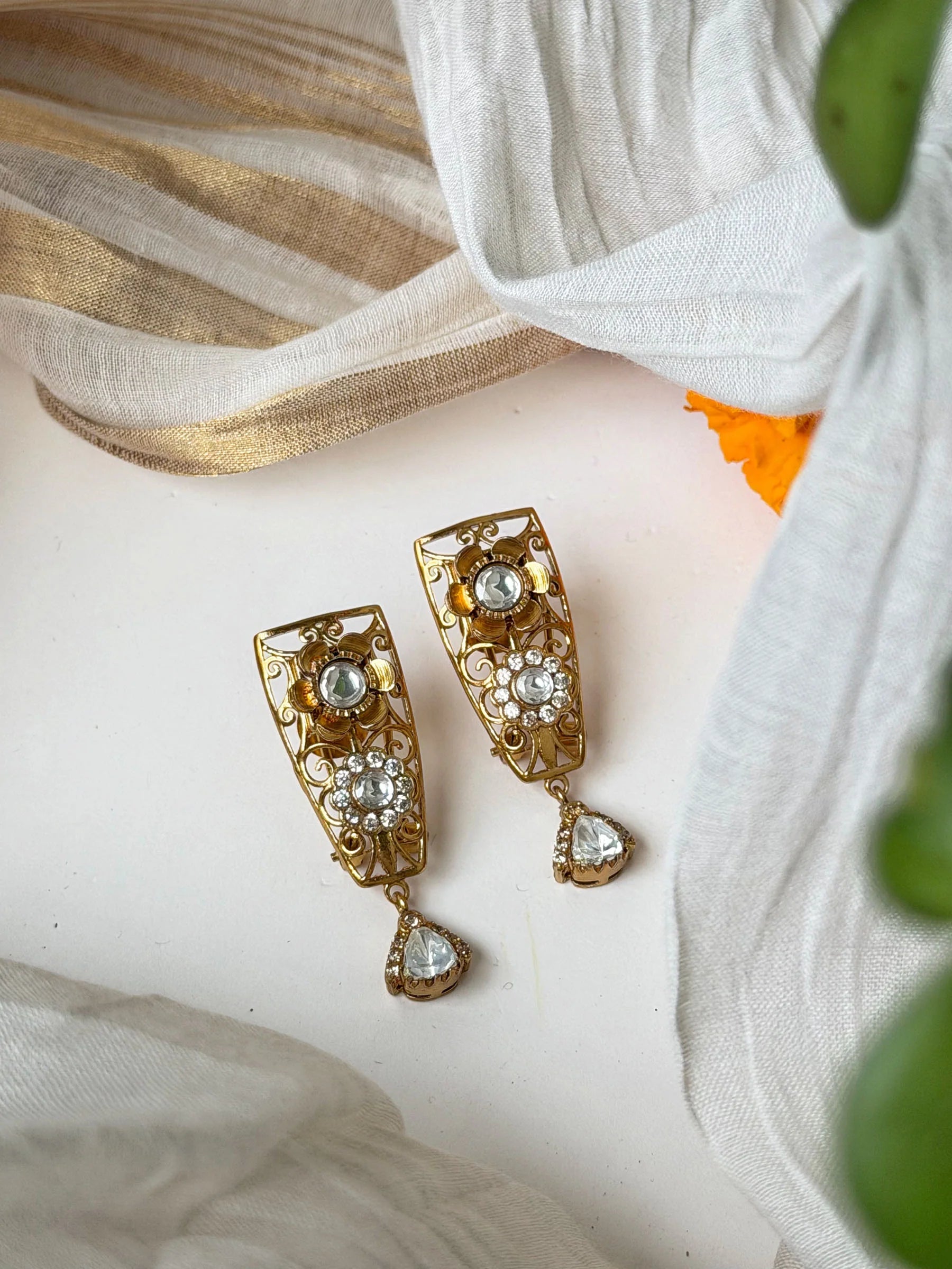 Traditional gold earrings with ornate detailing and hanging crystal drops in soft lighting

