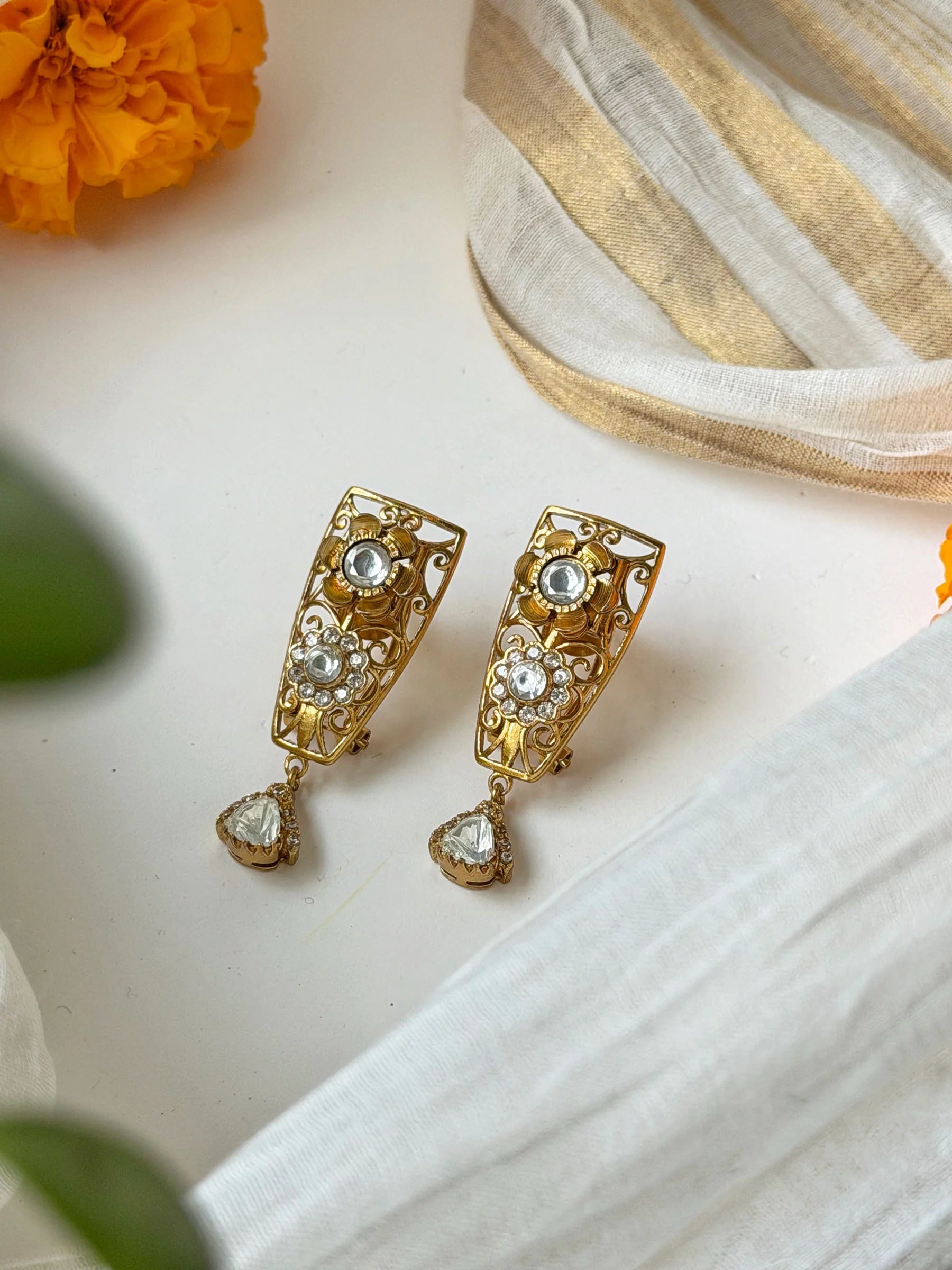 Luxury gold dangle earrings with floral motifs and clear gemstones in close-up view
