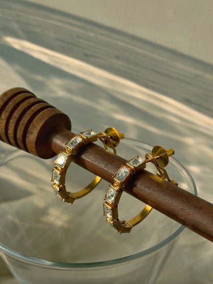 Luxury gold hoop earrings with geometric crystal accents styled on wooden stand with natural light
