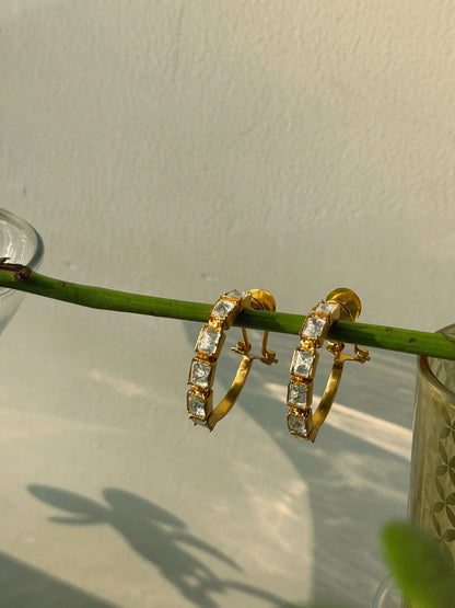 Stylish gold earrings with rectangular stones arranged on wooden bar with soft shadow patterns
