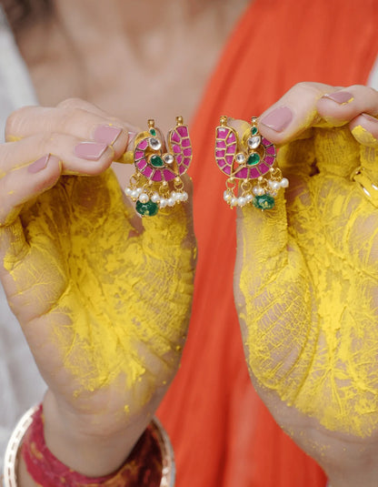 Fine jewelry close-up showcasing symmetrical earrings with colorful stonework and soft pearl drops against a vibrant fabric backdrop.
