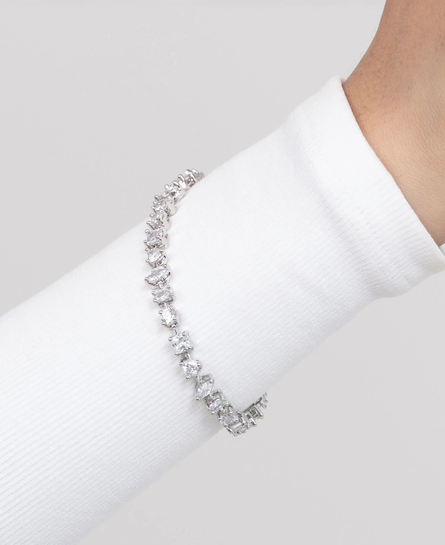 Elegant hand adorned with stacked rings and a tennis bracelet, gently gripping a green balloon with flowing ribbon.
