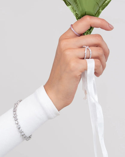 Minimal styling shot of a hand with fine diamond jewelry holding a glossy green balloon against a clean background.

