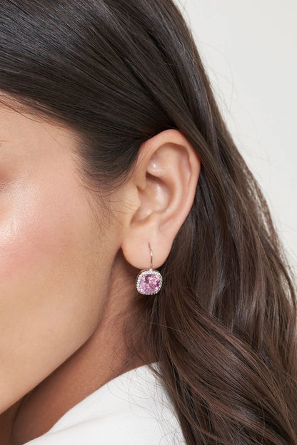 Close-up portrait of a woman wearing a pink gemstone drop earring set in white gold, highlighted against soft, natural makeup.
