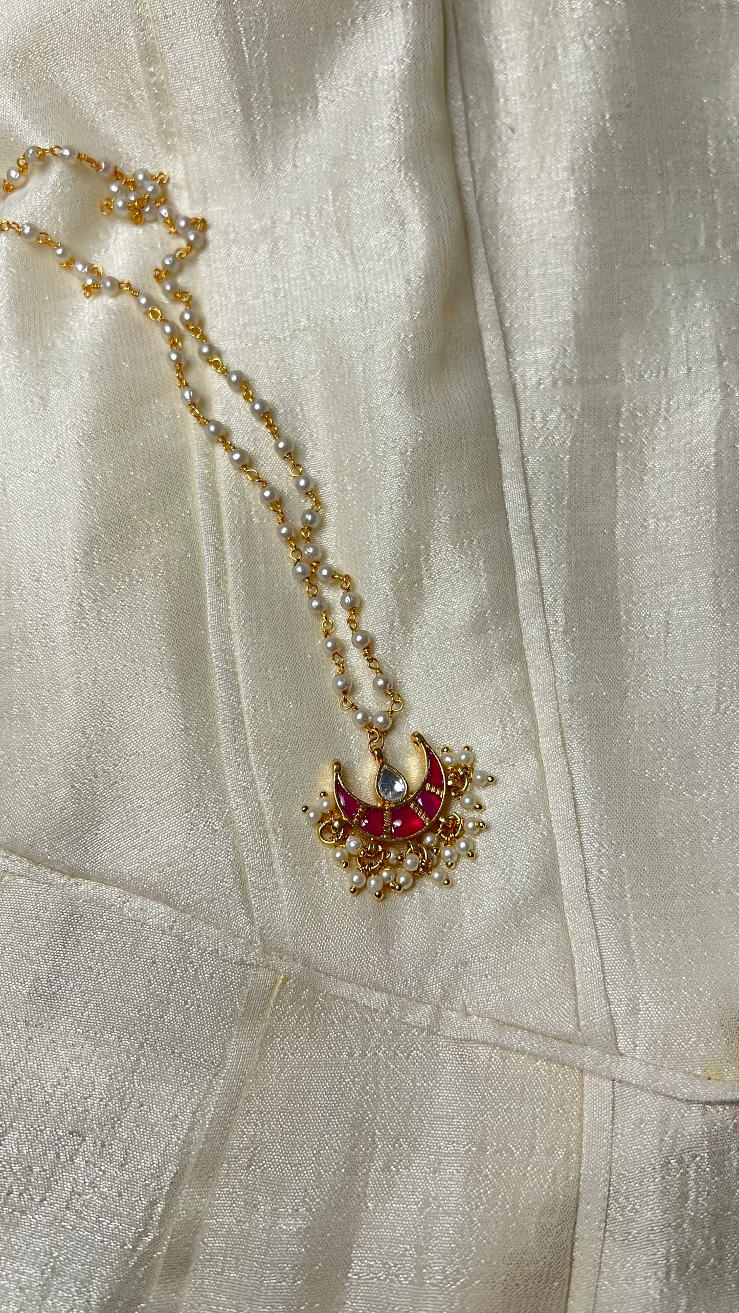 Sophisticated product shot of a traditional necklace with intricate enamel work and pearl detailing against a neutral textile backdrop.
