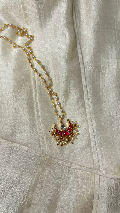 Sophisticated product shot of a traditional necklace with intricate enamel work and pearl detailing against a neutral textile backdrop.
