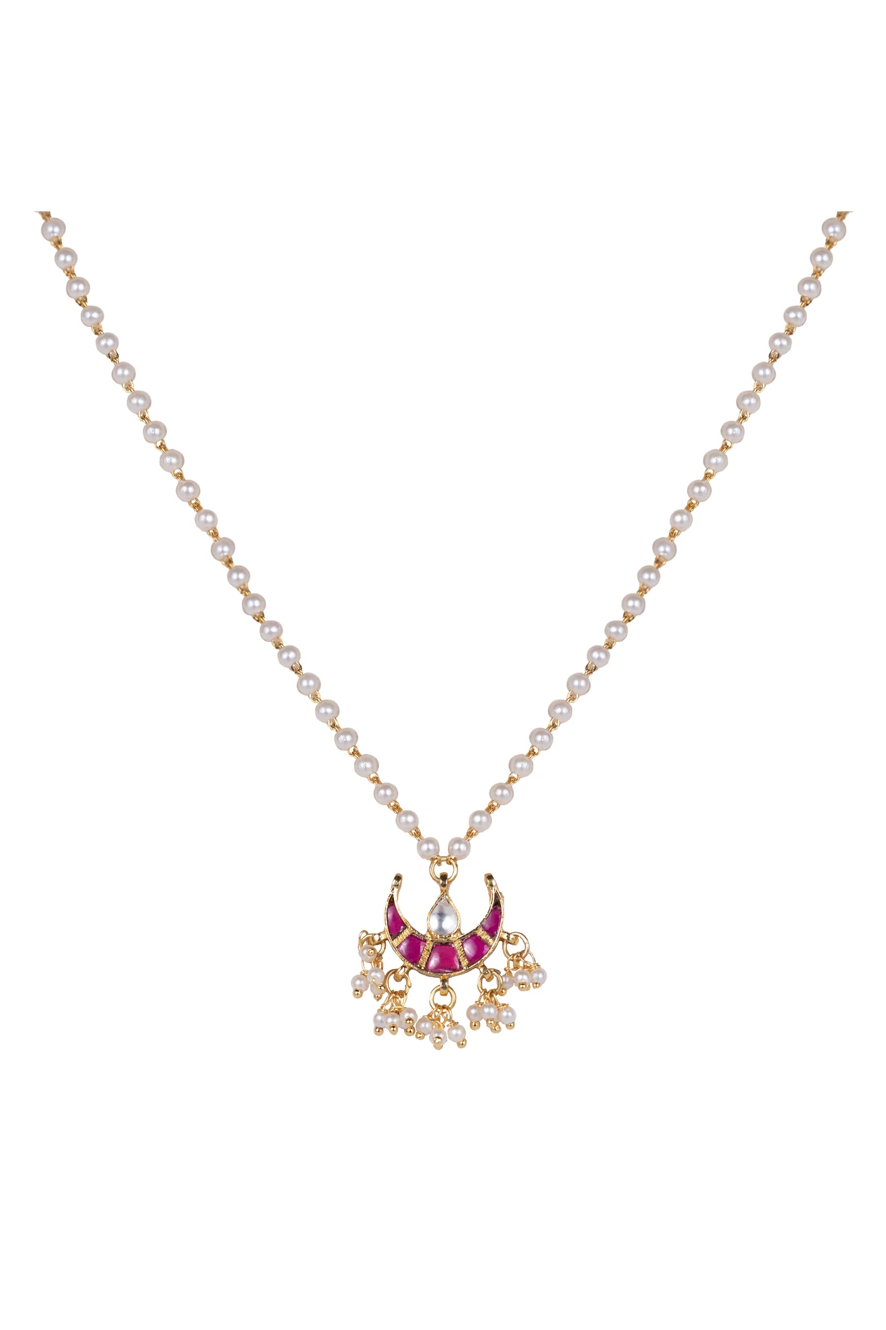 Detailed jewelry shot of a traditional-style necklace with gold beads, pearls, and a vibrant red pendant resting on textured fabric.
