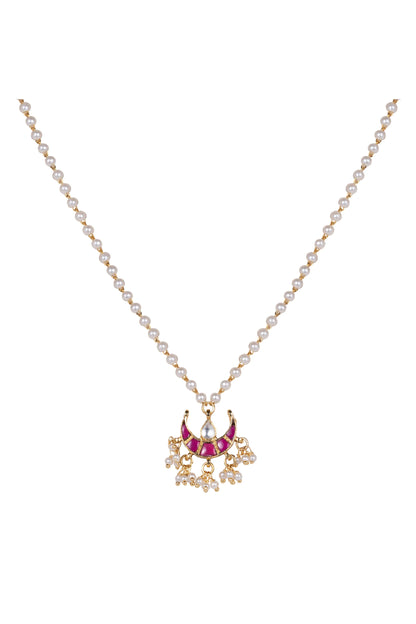 Detailed jewelry shot of a traditional-style necklace with gold beads, pearls, and a vibrant red pendant resting on textured fabric.
