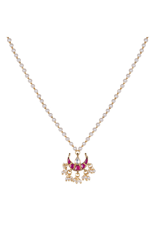Detailed jewelry shot of a traditional-style necklace with gold beads, pearls, and a vibrant red pendant resting on textured fabric.
