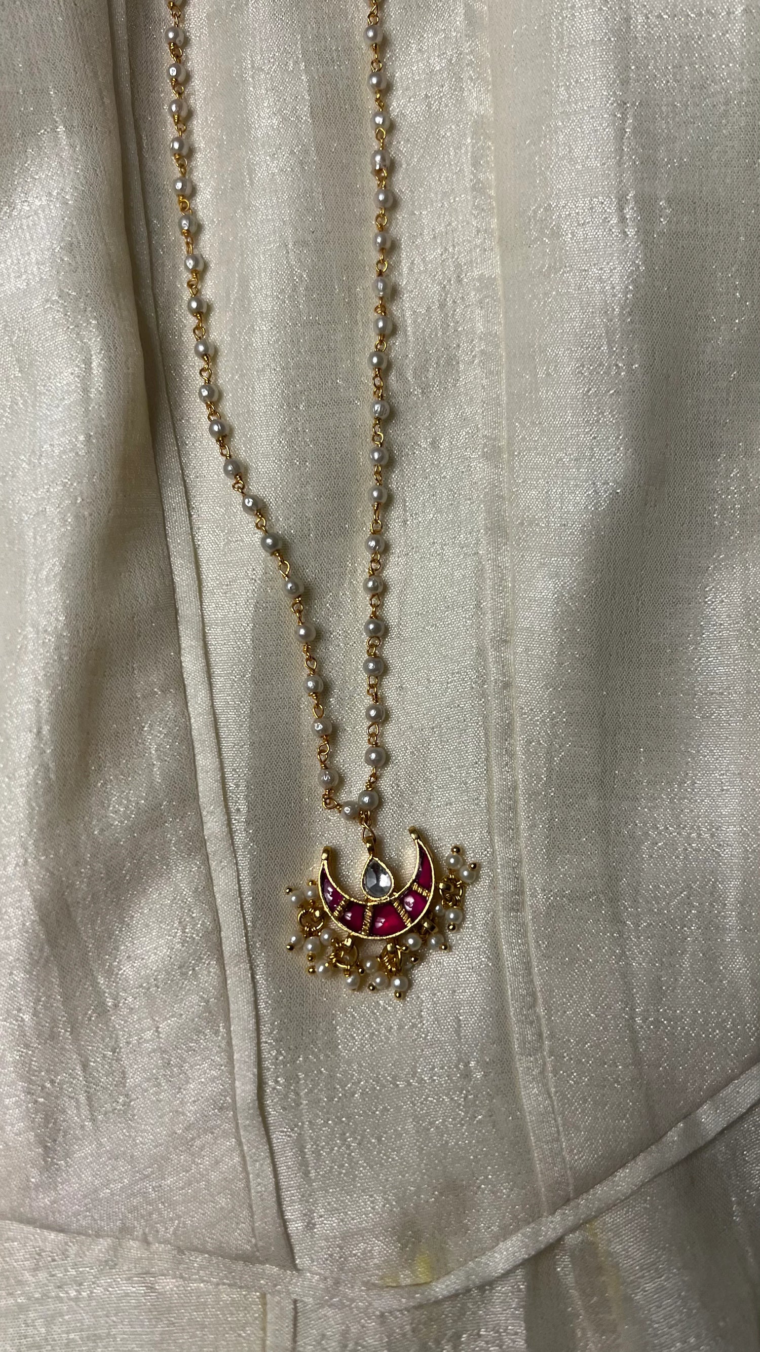 Minimal styling image highlighting a handcrafted necklace with pearl accents and a colorful crescent motif pendant.
