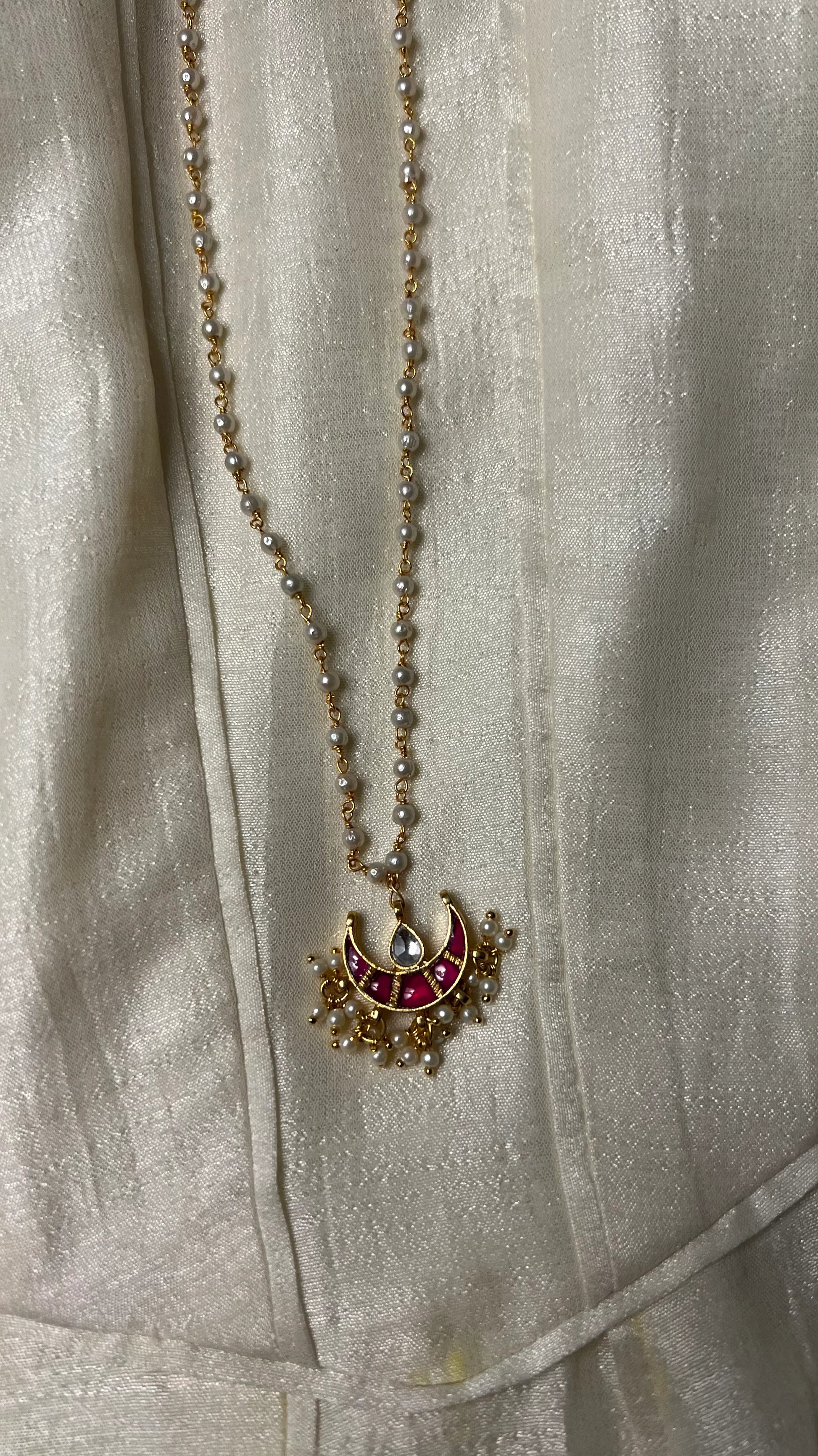 Minimal styling image highlighting a handcrafted necklace with pearl accents and a colorful crescent motif pendant.
