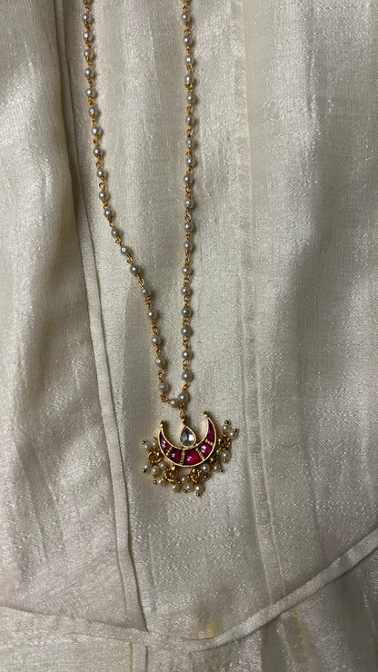 Minimal styling image highlighting a handcrafted necklace with pearl accents and a colorful crescent motif pendant.
