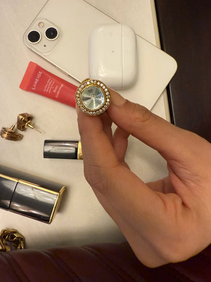 Elegant gold ring with oversized crystal stone showcased in hand with beauty products on table
