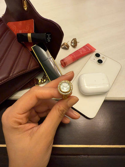 Close-up beauty scene with gold gemstone ring held in hand alongside lipstick and skincare items
