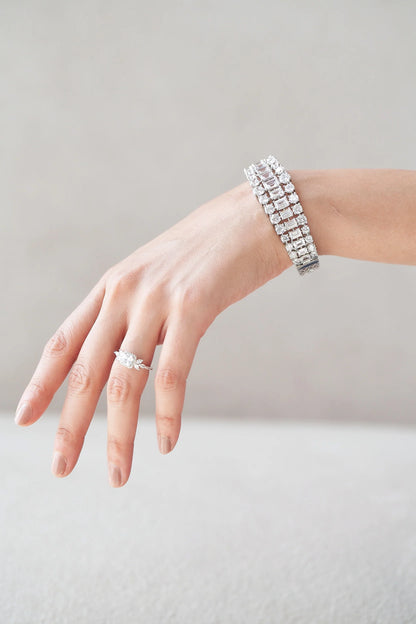 Fine jewelry composition with a cushion-cut diamond ring and a structured multi-row bracelet, both set in white gold on a relaxed pose.
