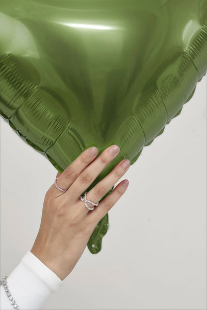 Close-up of a hand wearing delicate diamond rings while holding a large green leaf, blending fine jewelry with a natural backdrop.

