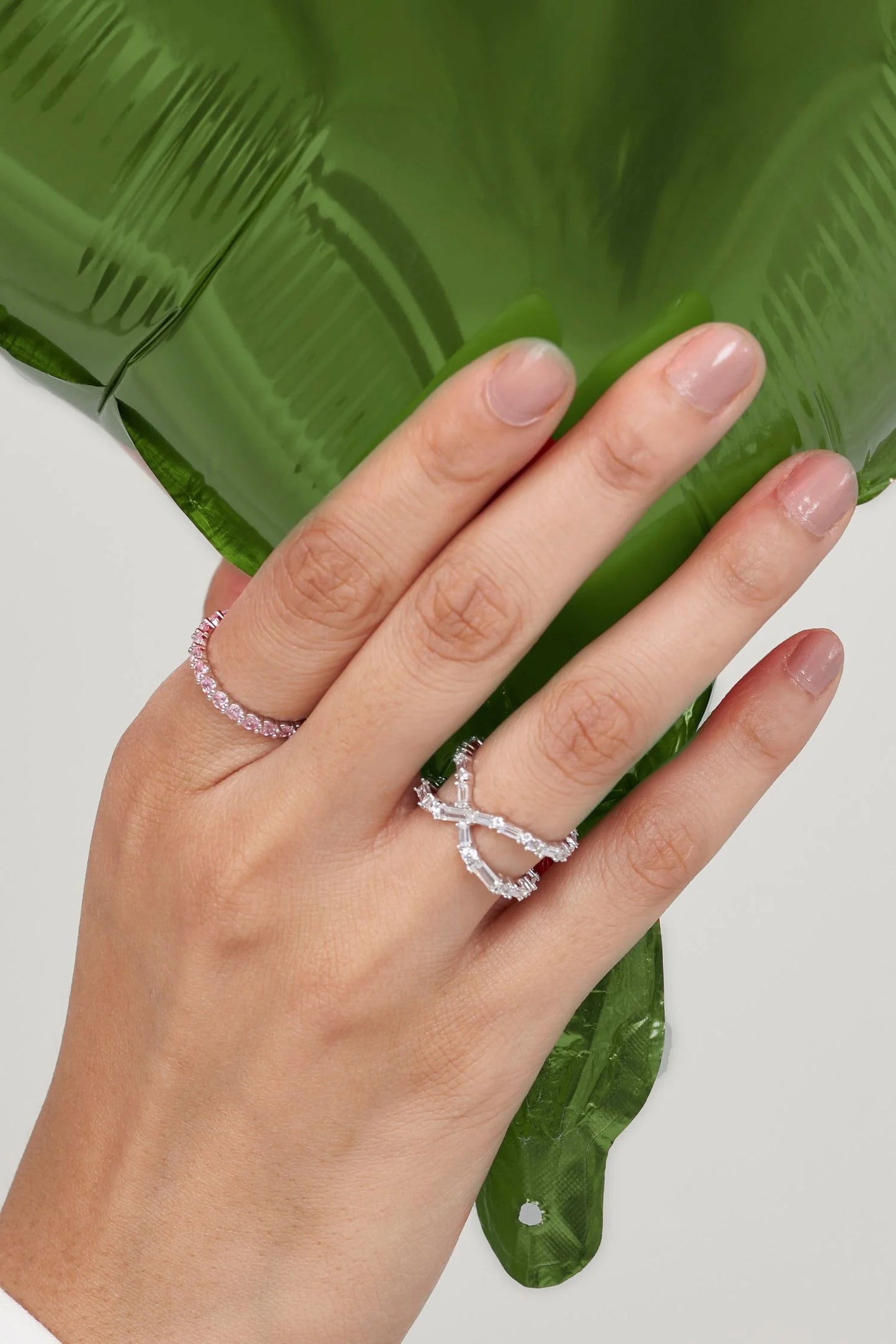 Elegant hand adorned with stacked diamond rings, gently placed against a glossy green leaf for a fresh, organic contrast.

