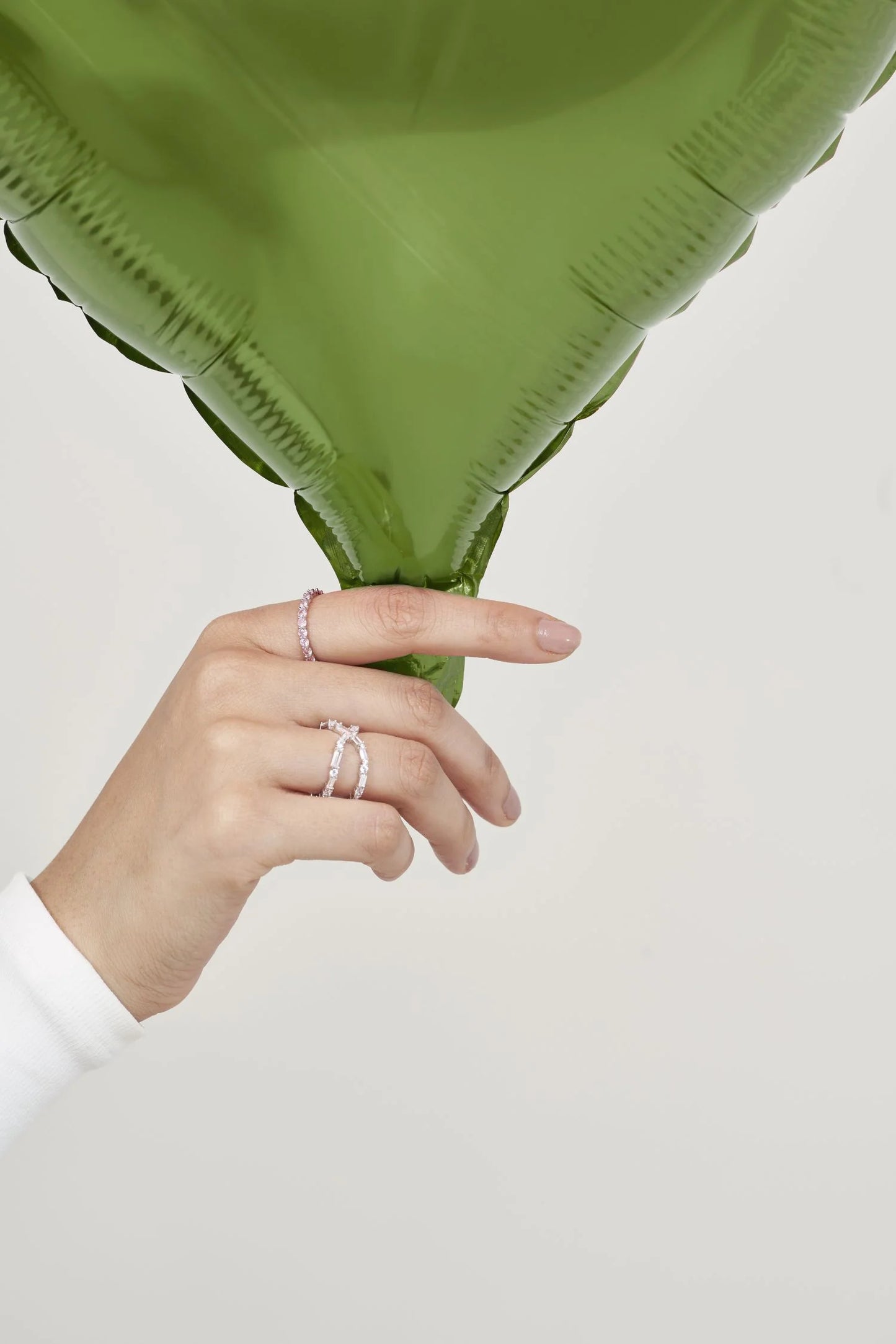 Fine jewelry detail featuring slim diamond bands and a statement ring, styled with a vibrant green leaf in a minimal setting.
