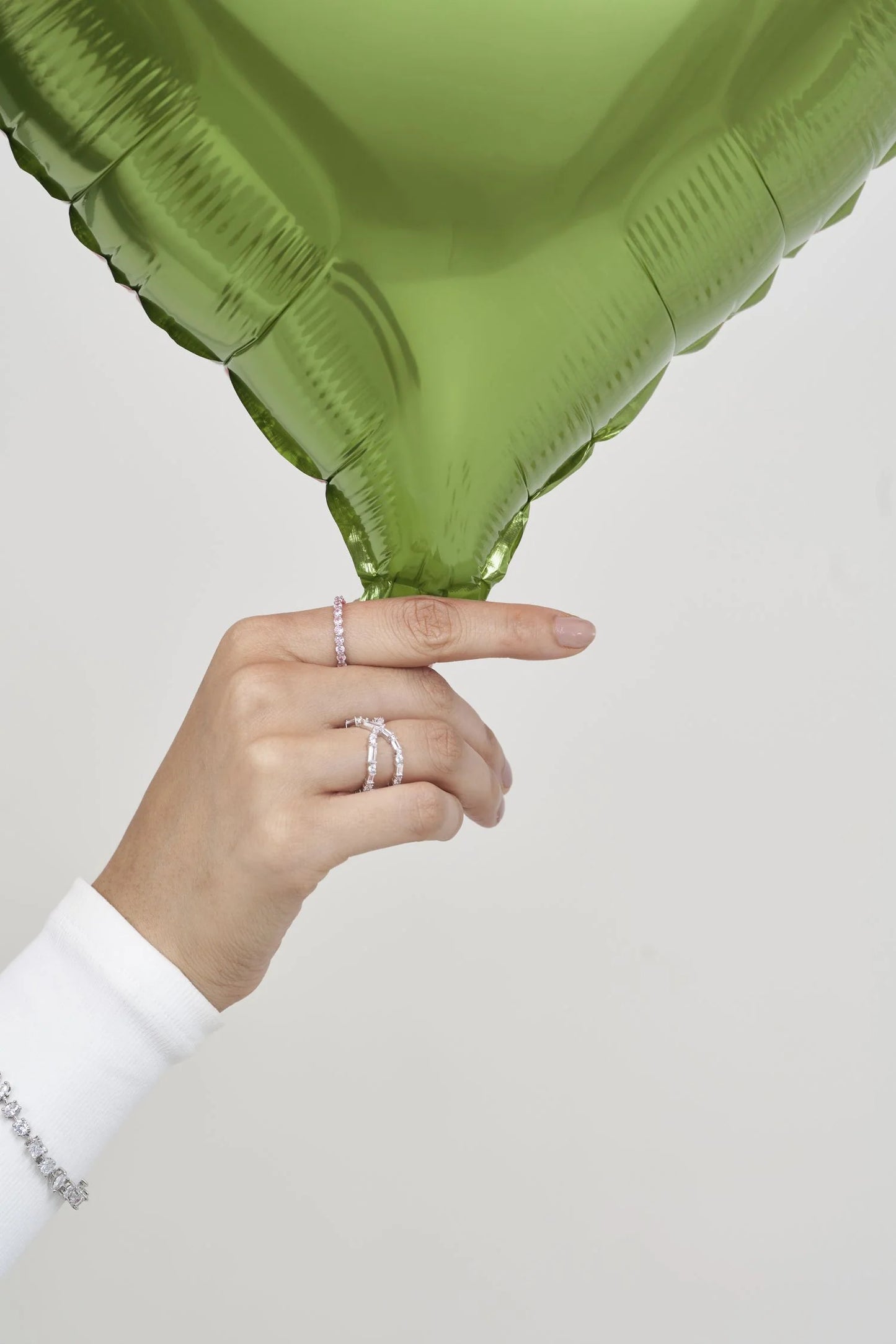 Close-up of manicured hand showcasing sparkling rings against a bold green botanical element for a modern editorial look.
