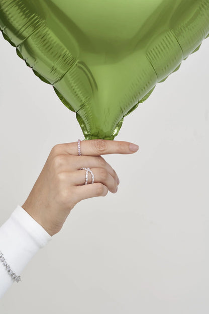 Close-up of manicured hand showcasing sparkling rings against a bold green botanical element for a modern editorial look.
