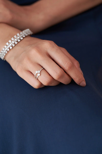 Fine white gold ring showcasing two brilliant-cut diamonds on a curved double band adorned with small accent stones.
